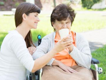 Jüngere Frau hilft älteren Frau im Rollstuhl beim Trinken