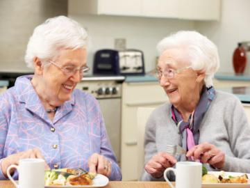 Zwei ältere Damen sitzen lachend beim Mittagessen am Tisch.